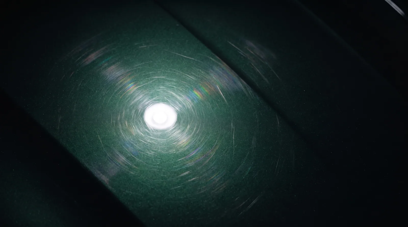 A green bonnet under one inspection lamp, its clear coat full of circular swirl marks.